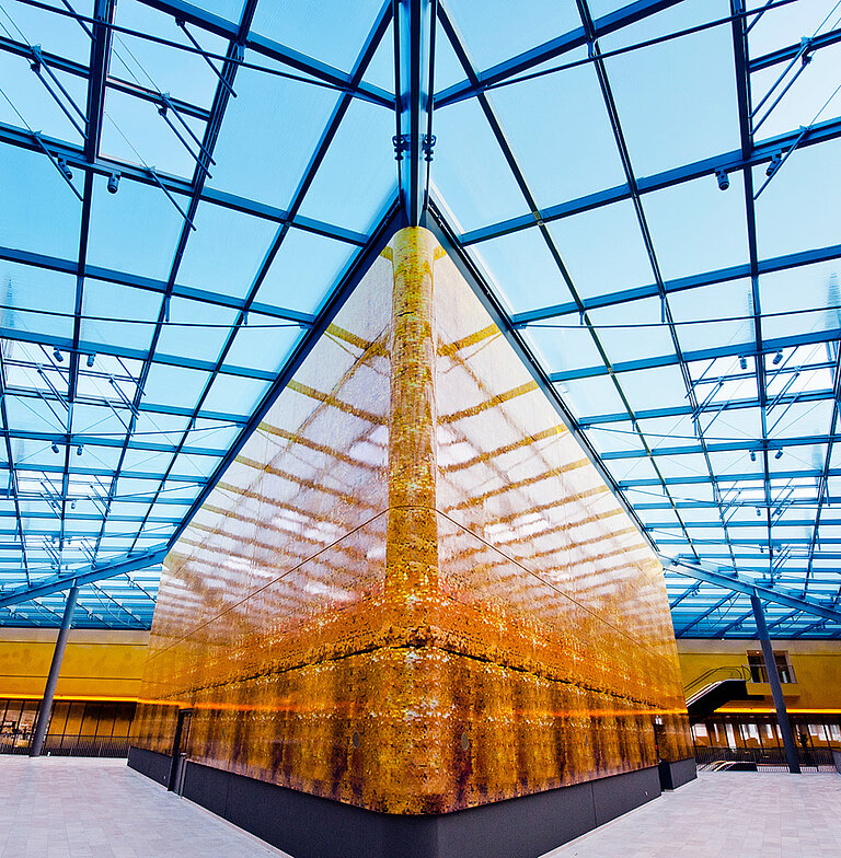 Großes Glasdach über einem goldenen Baukörper und Tageslichteinfall