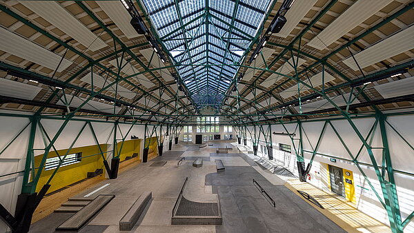 Historische Industriehalle mit Stahlträgern und großem Glasdach.