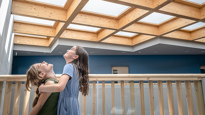 Zwei lachende Mädchen unter moderner Holz-Oberlichtdecke mit Tageslichteinfall