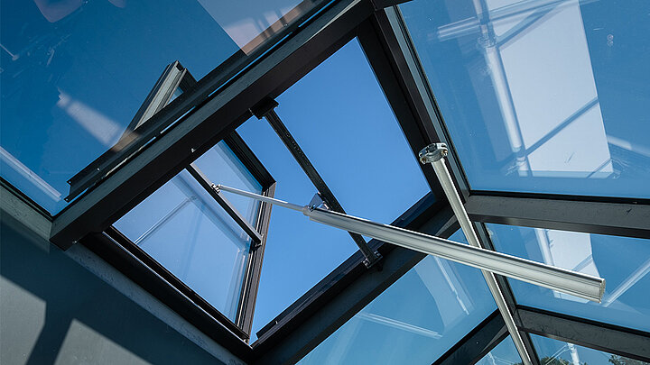 Geöffnetes Dachfenster mit Aluminiumrahmen und silbernen Stützstreben vor blauem Himmel