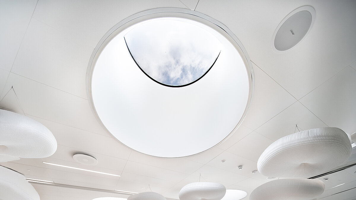 Rundes Oberlicht in der Decke des Ernst & Young Bürogebäudes mit Blick in den Himmel und modernen, schwebenden Leuchtelementen