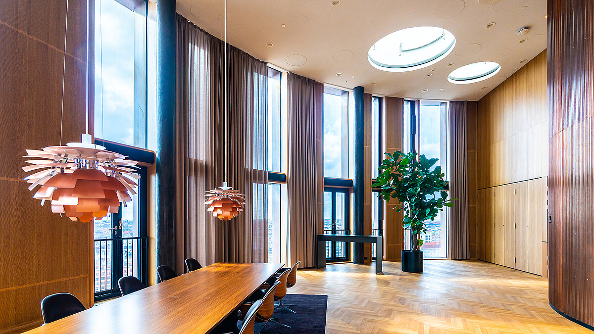 Heller Konferenzraum mit großem Holztisch, bodentiefen Fenstern und zwei runden Oberlichtern