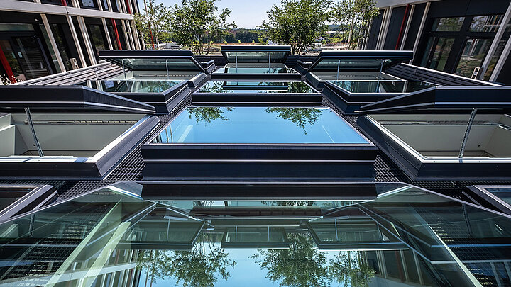 Modernes Glasdach mit Stahlkonstruktion Spiegelungen von Bäumen und blauem Himmel