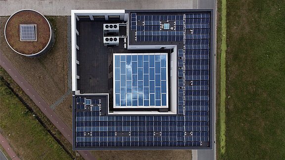 Luftaufnahme eines Flachdachs mit zentralem Glasdach und umliegenden Solarmodulen