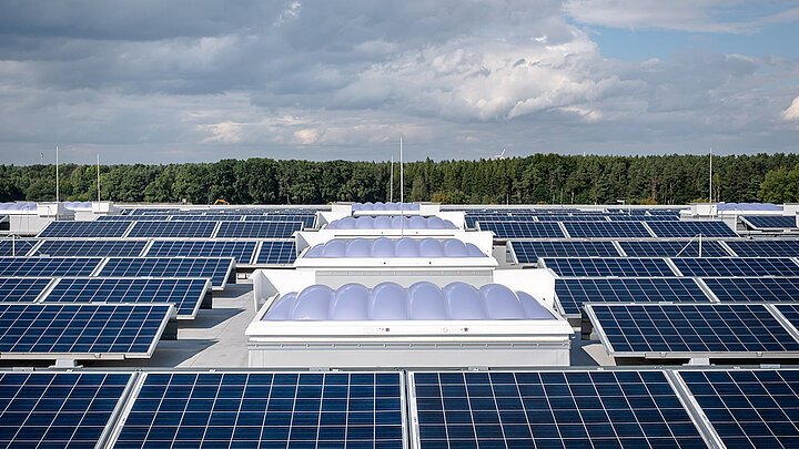 Flachdach mit zahlreichen Solarmodulen und integrierten Lichtkuppeln vor bewaldeter Landschaft