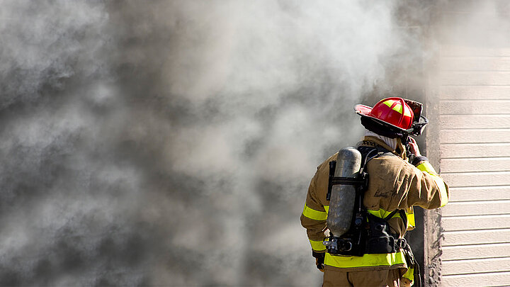 Feuerwehrmann vor brennendem Gebäude mit Brandrauch