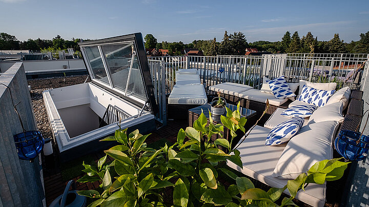 Dachterrasse mit Dachausstieg, Terrassenmöbeln, Pflanzen und blauem Himmel