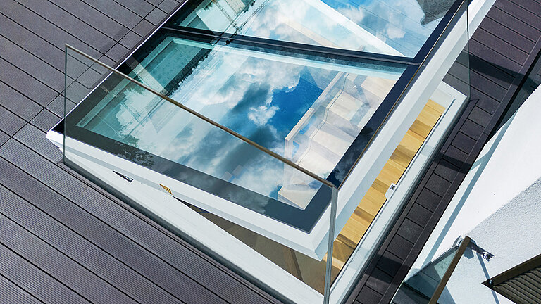Moderner Flachdach Ausstieg mit Spiegelung von blauem Himmel und Wolken, Glasgeländer und Holzterrasse