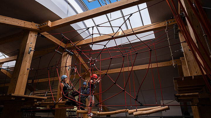 Indoor-Kletterparcours mit Holzträgern, rotem Kletternetz und Oberlicht
