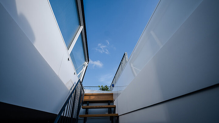 Treppe führt durch einen Flachdach Ausstieg auf die Dachterrasse mit blauem Himmel.