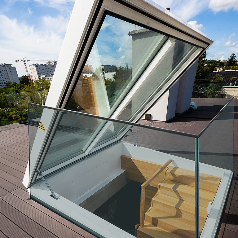 Geöffneter Flachdach Ausstieg mit Holztreppe und Glasgeländer auf moderner Dachterrasse mit Stadtblick