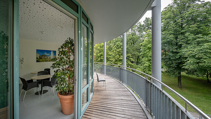 Geschwungener Balkon mit Blick ins Grüne, angrenzend an ein modernes Büro mit Glasfront.