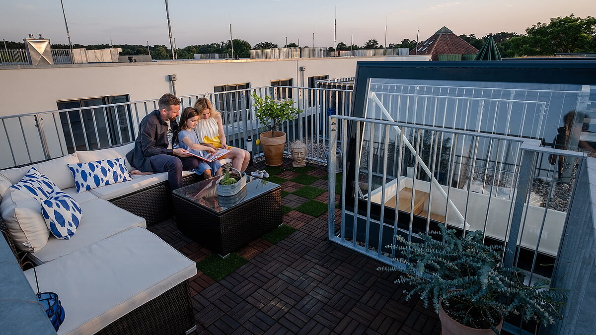 Familie sitzt bei Sonnenuntergang auf der Dachterrasse von ihrem Townhouse in Berlin mit Flachdach Ausstieg