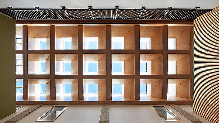 Innenansicht eines Atriums mit Holzlamellen und quadratischen Fensteröffnungen