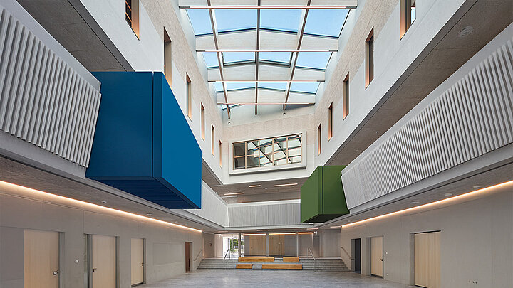 Modernes Atrium mit Oberlicht, wellenförmigen Wänden und farbigen Box-Elementen.