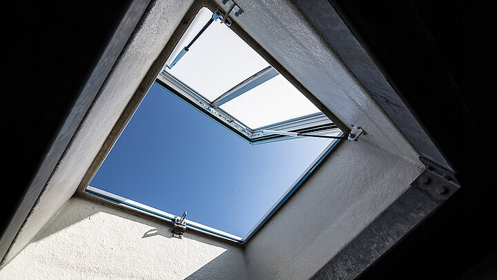 Geöffnetes Dachfenster mit Blick in blauen Himmel