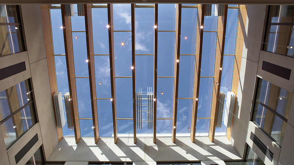 Modernes Atrium mit vertikalen Holzlamellen und großem Glasdach mit Blick in den Himmel