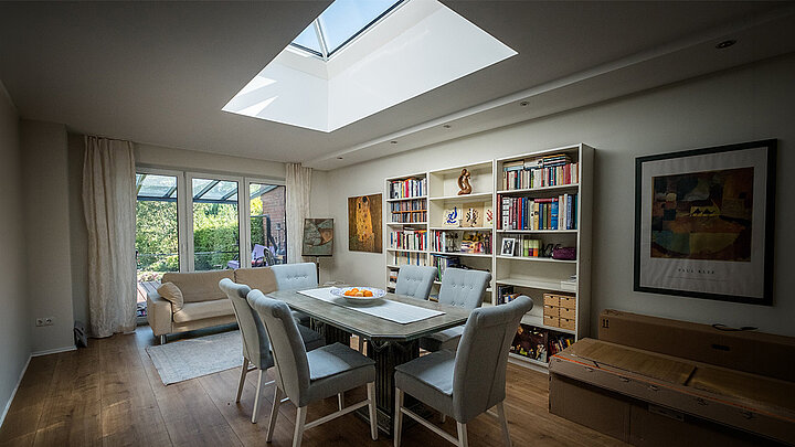 Wohn- und Esszimmer mit großem Dachfenster, Esstisch, Bücherregalen und Blick in den Garten.
