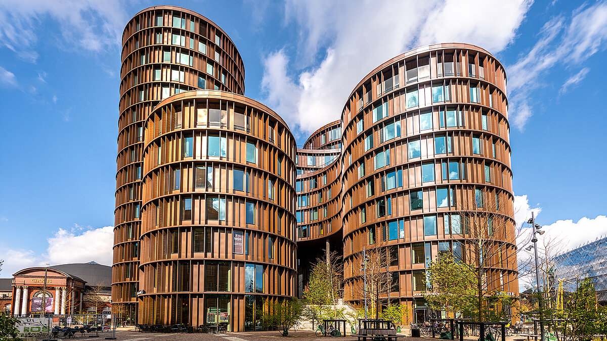 Moderne Wohngebäude mit geschwungener Fassade und großen Fensterflächen unter blauem Himmel
