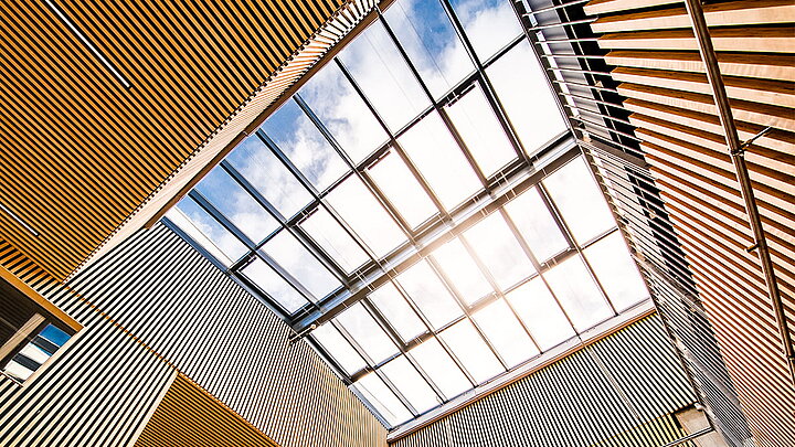 Architektonisch auffälliges Glasdach mit wellenförmigen Holzelementen und Sonnenlicht.