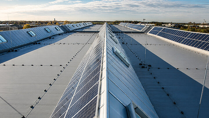 Industriehalle mit großflächiger Dachkonstruktion und installierten Solarmodulen unter blauem Himmel