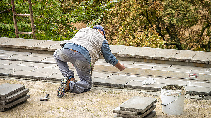 Handwerker verlegt Terrassenplatten auf Stelzlagern bei der Montage einer Dachterrasse