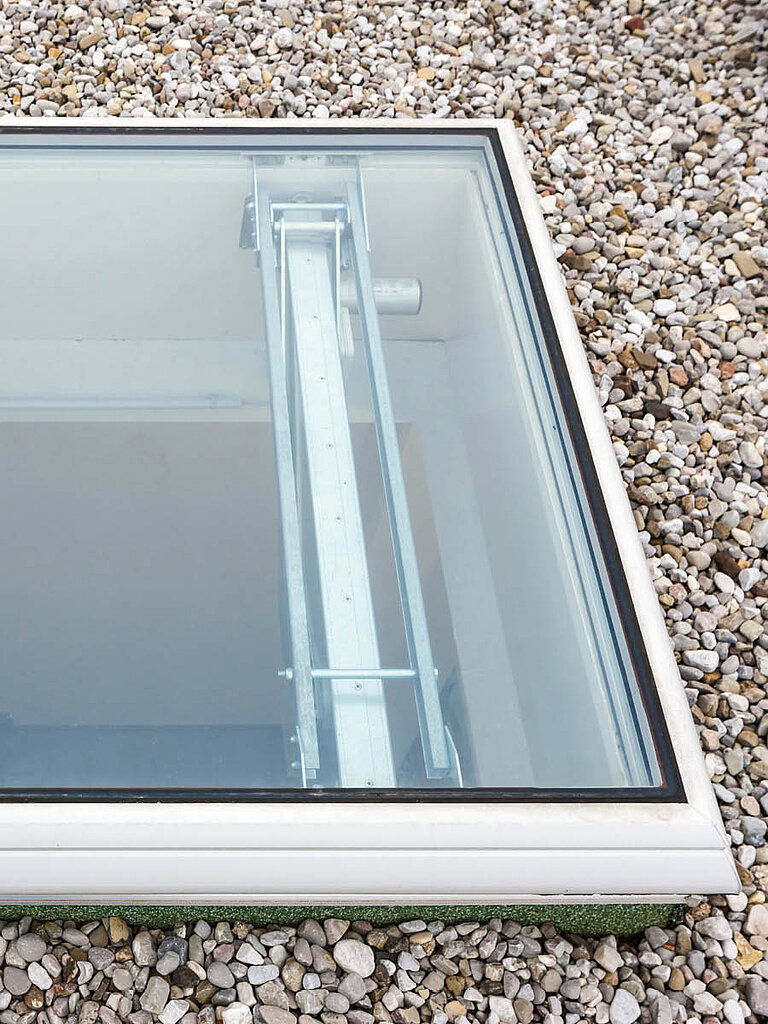 Detailansicht eines LAMILUX Flachdach Fenster F100 RWA auf Kies-Flachdach mit transparenter Verglasung und sichtbarer Antriebstechnik