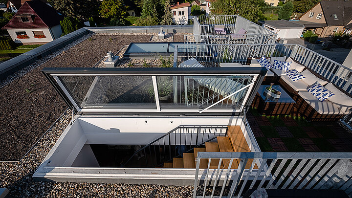 Moderne Dachterrasse mit Glasluke, Holztreppe, Lounge-Möbeln und grüner Bodenverkleidung.
