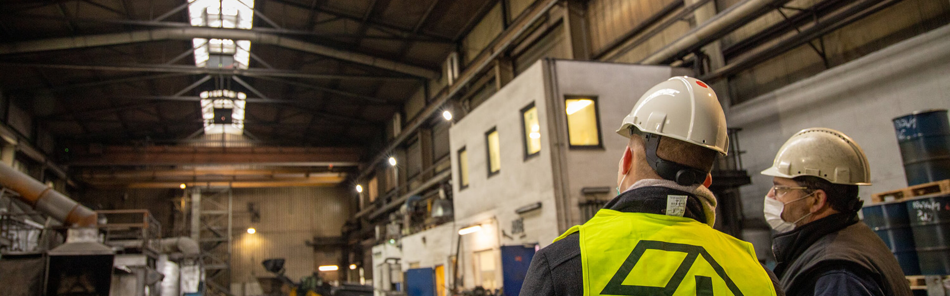 Bauarbeiter mit Helm und Warnweste blickt in große Industriehalle mit LAMILUX Lichtband