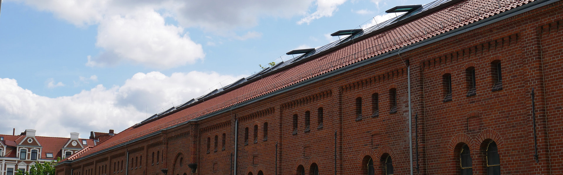 Rotes Ziegeldach mit zahlreichen Solarpanels auf historischem Backsteingebäude.