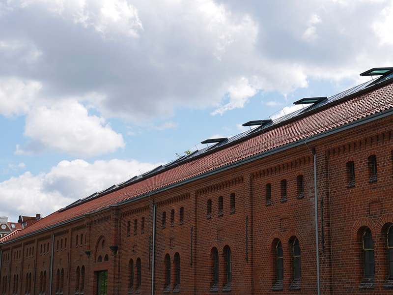 Rotes Ziegeldach mit zahlreichen Solarpanels auf historischem Backsteingebäude.
