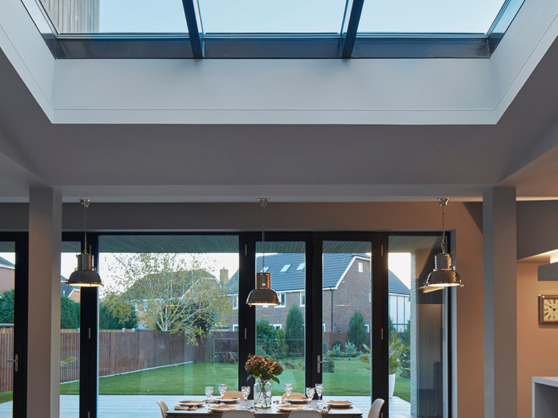 Moderner Essbereich mit Blick durch große Glasfront auf Garten im Abendlicht.