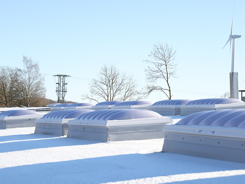 Flachdach mit Schneedecke und Lichtkuppeln bei sonnigem Wetter.