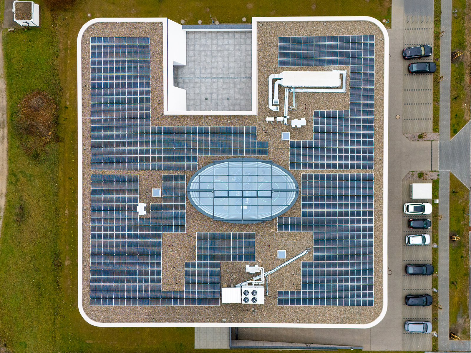 Luftaufnahme eines Industriegebäudes mit großflächiger Photovoltaikanlage und zentralem ovalem Dachbereich