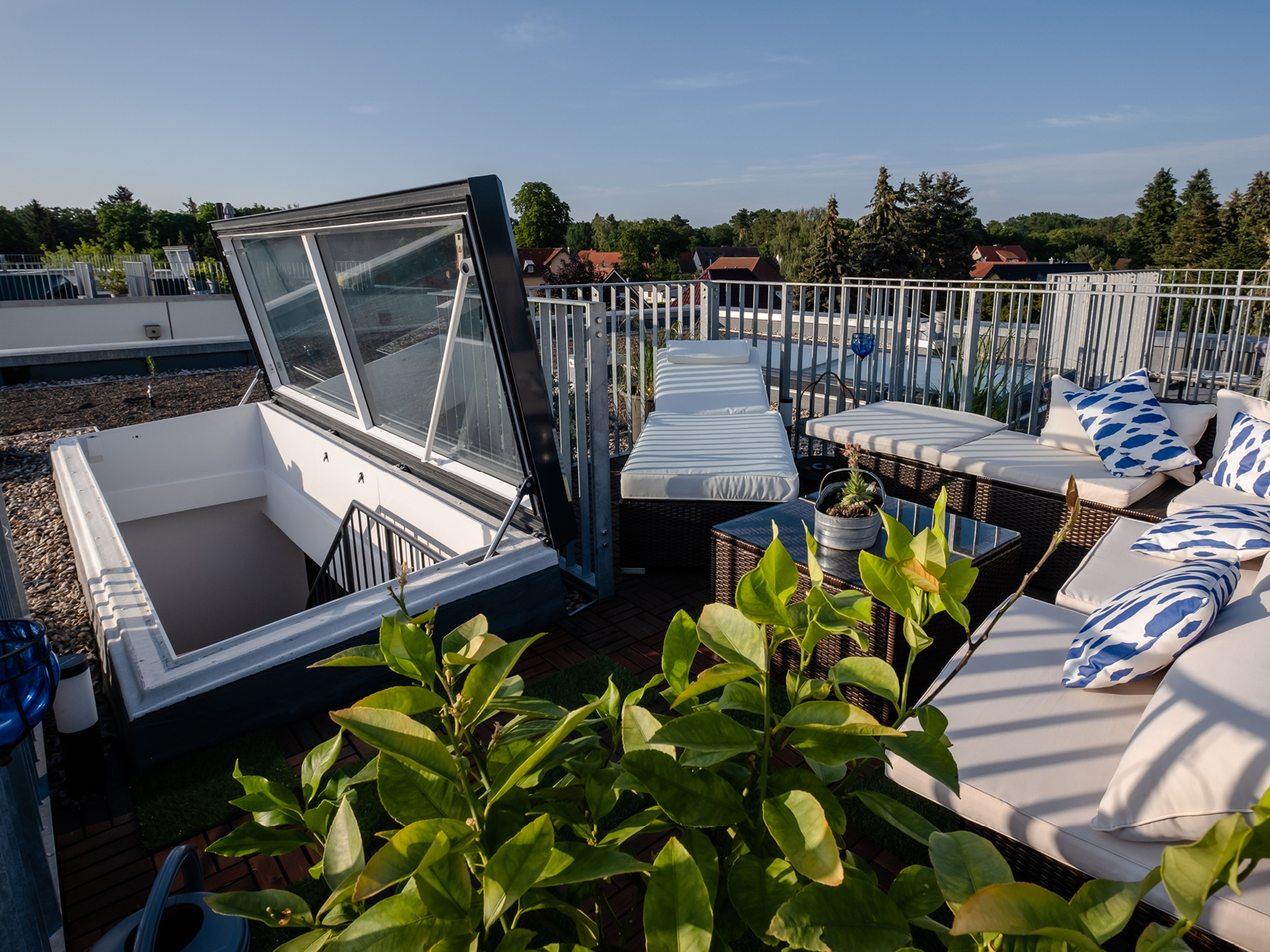 Stilvolle Dachterrasse mit Lounge-Möbeln, weißen Polstern, blauen Kissen und Zugang über einen modernen Dachausstieg.