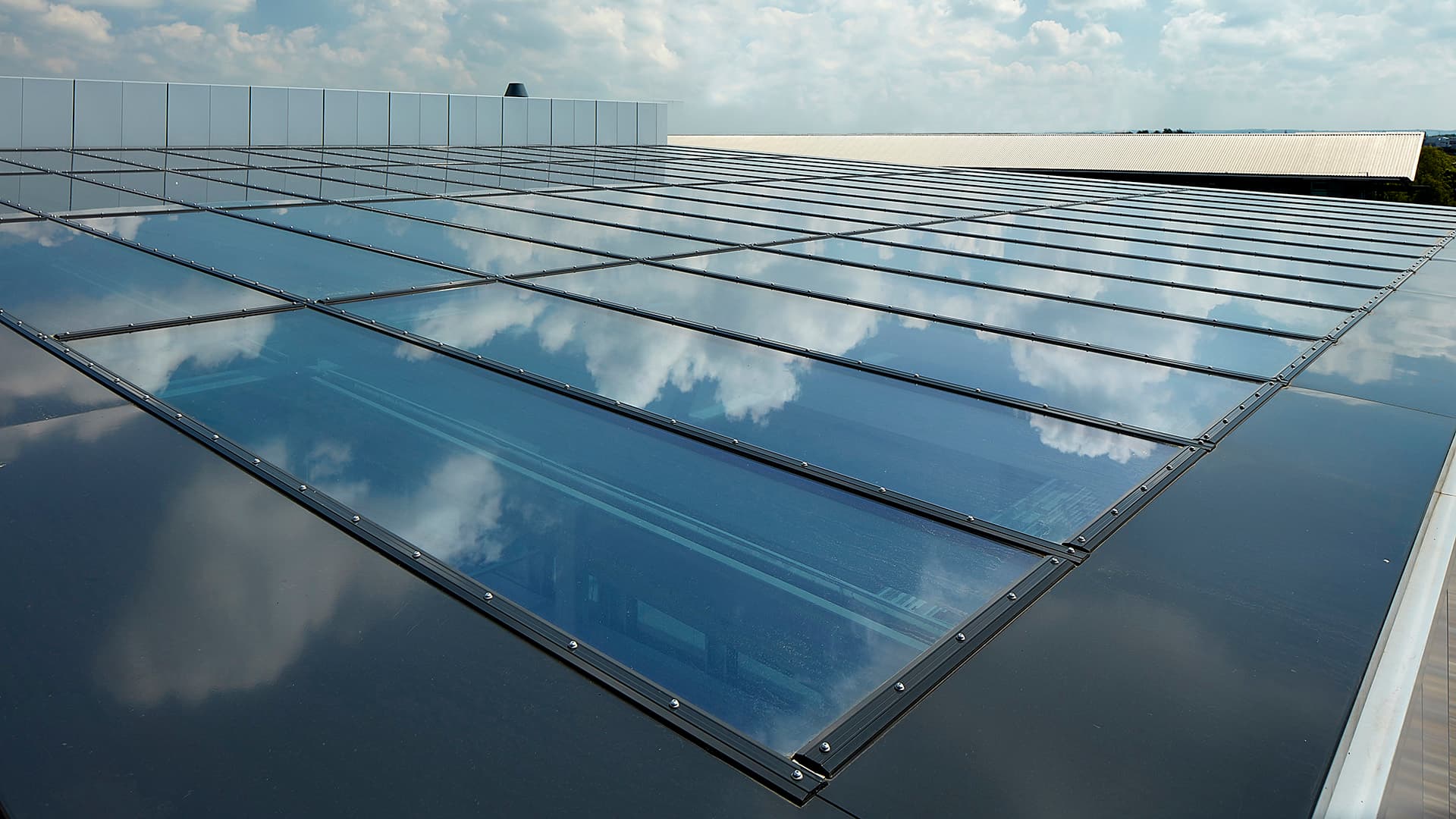 Glasdach der Gewerbeimmobilie im Milton Park, England, mit reflektierendem Himmel und Wolken auf der Oberfläche.